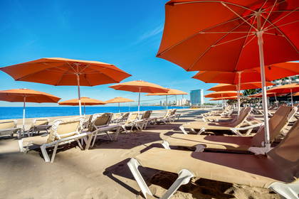 Plaża z pomarańczowymi parasolami i leżakami.