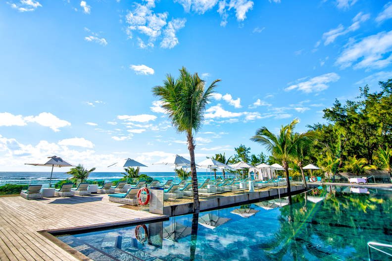 Basen z leżakami i palmami z widokiem na ocean.