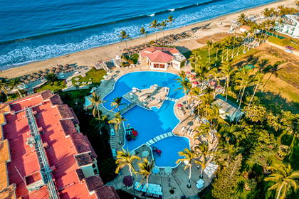 Hotel z basenem, plażą i palmami sfotografowany z lotu ptaka.