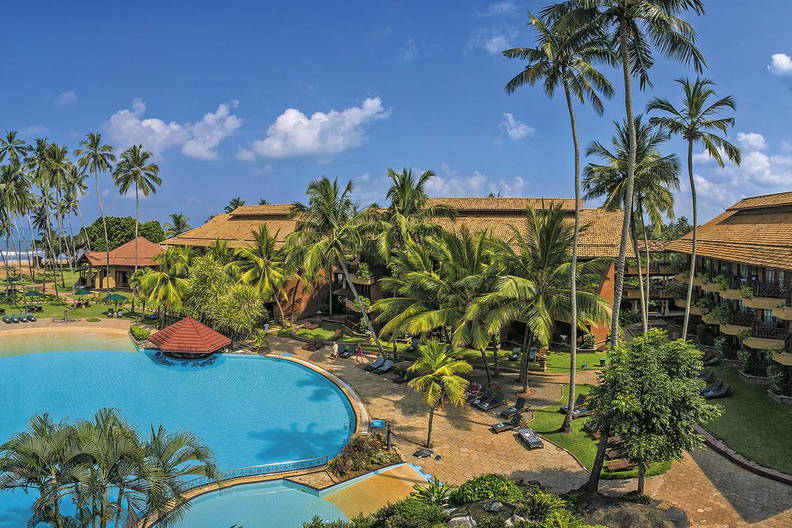 Hotel z basenem i palmami w słoneczny dzień.