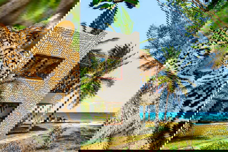 Głowa leoparda na pierwszym planie i willa z widokiem na ocean w tle.