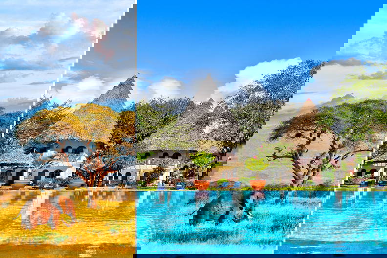 Słoń na sawannie i hotel z basenem w tle.