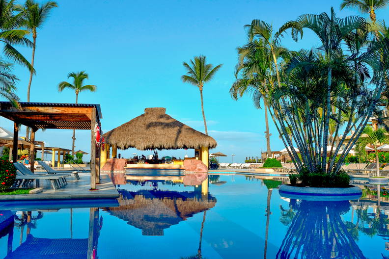 Basen z barami pod strzechą i palmami w tropikalnym kurorcie.