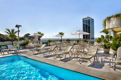 Basen na dachu budynku z widokiem na ocean i miasto. Na dachu leżaki i parasole.