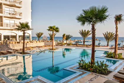 Kompleks hotelowy z basenem, palmy i widok na morze.