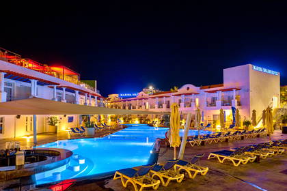 Hotel z basenem oświetlony nocą. Widoczne leżaki.