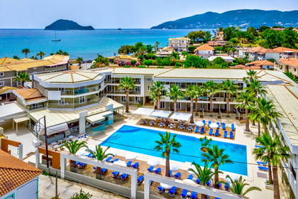 Hotel z basenem, leżakami i palmami. Widok z góry. W tle morze i góry.