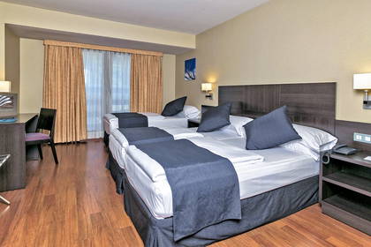 Pokój hotelowy z trzema pojedynczymi łóżkami, biurkiem i drewnianą podłogą.