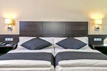 Pokój hotelowy z dwoma łóżkami i ciemnym zagłówkiem.