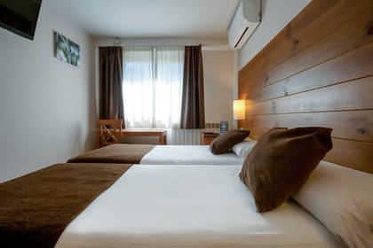 Pokój hotelowy z dwoma łóżkami, drewnianym zagłówkiem i brązowymi zasłonami.