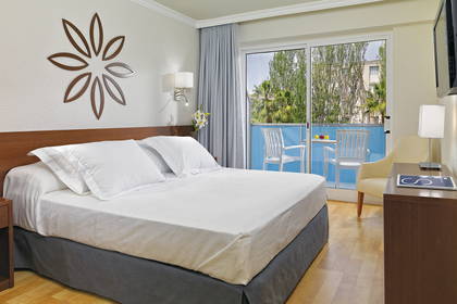 Pokój hotelowy z balkonem i widokiem na zieleń. Widoczne łóżko.
