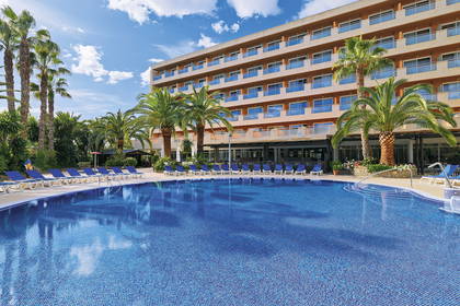 Hotel z basenem i palmami w słoneczny dzień.