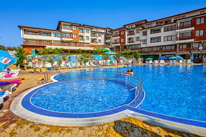 Kompleks hotelowy z basenem i relaksującymi się gośćmi.