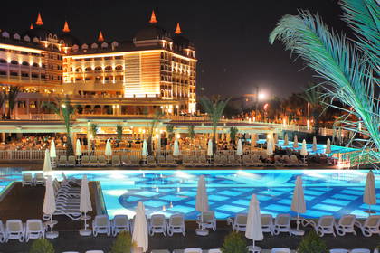 Oświetlony nocą hotel z basenem i leżakami.
