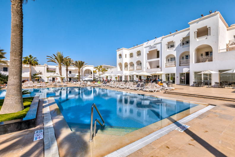 Kompleks hotelowy z basenem otoczonym palmami.