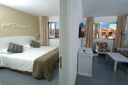 Widok na pokój hotelowy z łóżkiem i częścią wypoczynkową, widziany zza drzwi.