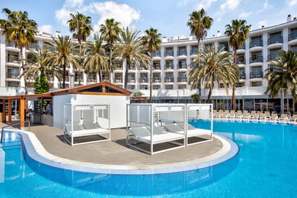 Basen hotelowy z leżakami pod baldachimami, w tle palmy.