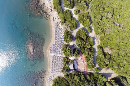Widok z góry na plażę z parasolami, morze i las.