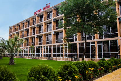 Hotel Riva z zewnątrz, otoczony trawnikiem i zielenią.