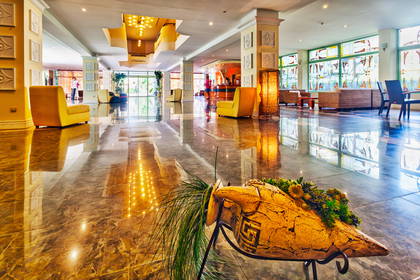 Lobby hotelowe z marmurową podłogą, fotelami i ozdobną urną.
