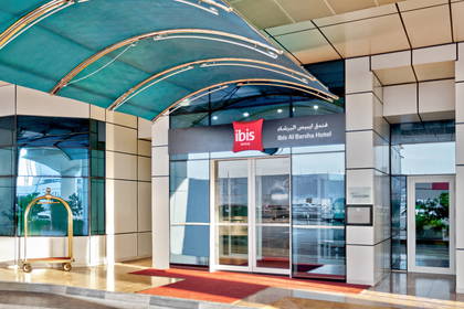Wejście do hotelu Ibis Al Barsha i wózek bagażowy.