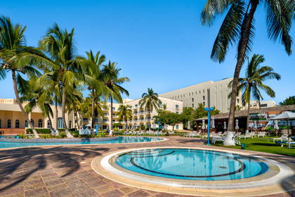 Hotel z basenem i palmami w słoneczny dzień.