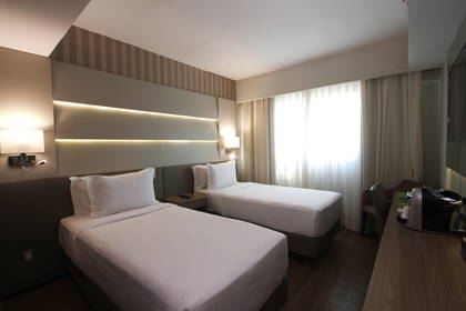 Pokój hotelowy z dwoma pojedynczymi łóżkami, lampami i biurkiem.