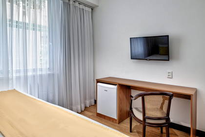 Pokój hotelowy z telewizorem, biurkiem i zasłonami w oknach.