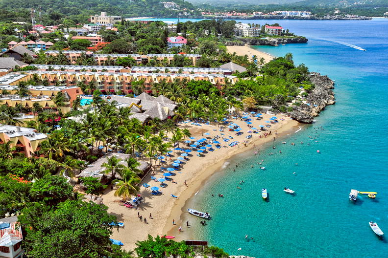 Widok z lotu ptaka na tropikalny kurort: plaża, błękitna woda i palmy.