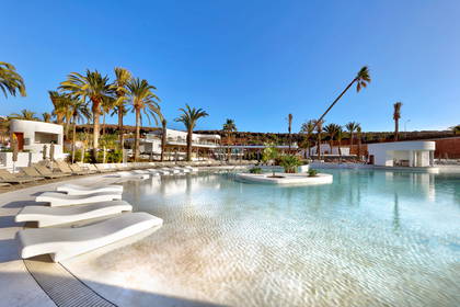 Resort z basenem i leżakami otoczony palmami.