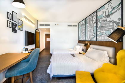 Pokój hotelowy z dwoma łóżkami, biurkiem i żółtym fotelem.