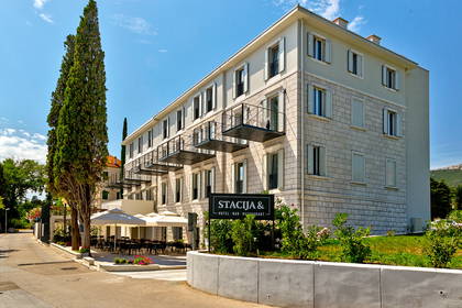 Trzypiętrowy hotel z balkonami i restauracją na świeżym powietrzu.