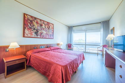 Pokój hotelowy z czerwonym łóżkiem, szafką nocną i balkonem.