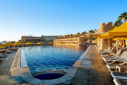 Kompleks hotelowy z basenem, leżakami i parasolami.