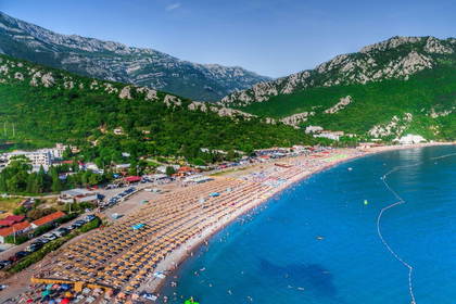 Plaża z parasolami, turkusowa woda i góry w tle – widok z lotu ptaka.