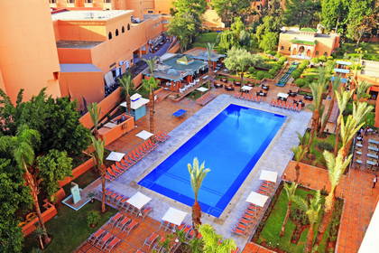 Hotel z basenem, leżakami i palmami, widok z góry.