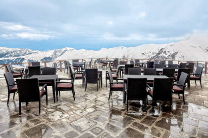 Pusty taras restauracyjny z widokiem na ośnieżone góry pod pochmurnym niebem.