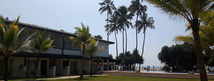 Hotel z palmami i basenem, z widokiem na plażę.