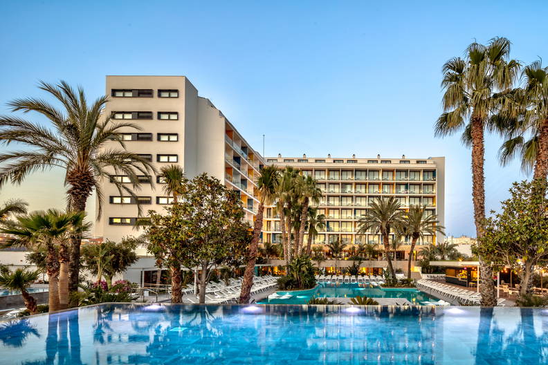 Kompleks hotelowy z basenem otoczonym palmami.