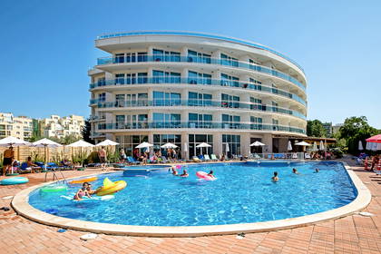 Hotel z basenem wypełnionym ludźmi w słoneczny dzień.