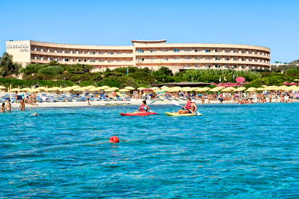 Plaża, hotel w tle i kajakarze na wodzie.