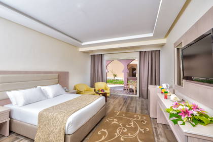 Jasny pokój hotelowy z łóżkiem, balkonem i kwiatami w wazonie.
