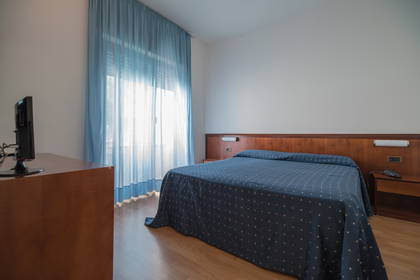 Pokój hotelowy z łóżkiem, szafką nocną i zasłonami w oknach.
