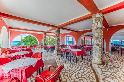 Restauracja z widokiem na morze. Wnętrze lokalu wypełniają czerwone stoły i kamienne kolumny.