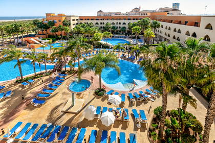 Widok z góry na hotelowy basen z leżakami i palmami.