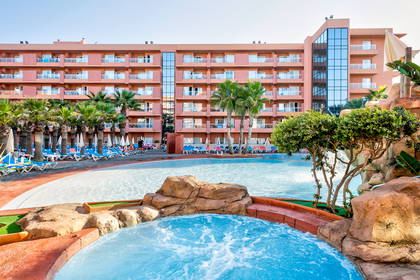 Kompleks hotelowy z basenem, palmami i leżakami do opalania.