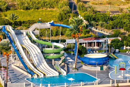 Widok z lotu ptaka na aquapark z kolorowymi zjeżdżalniami, basenami i palmami.