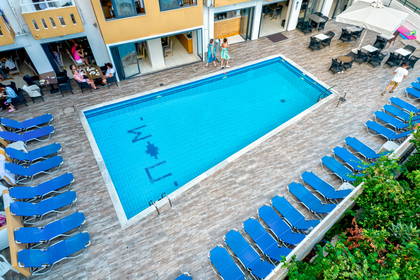 Basen otoczony leżakami i budynkami hotelowymi, widok z góry.