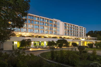 Nowoczesny, oświetlony nocą biały hotel z balkonami.