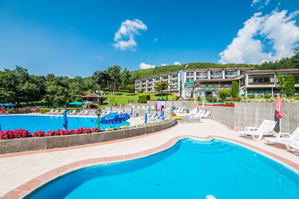 Basen hotelowy z leżakami i budynkiem w tle.